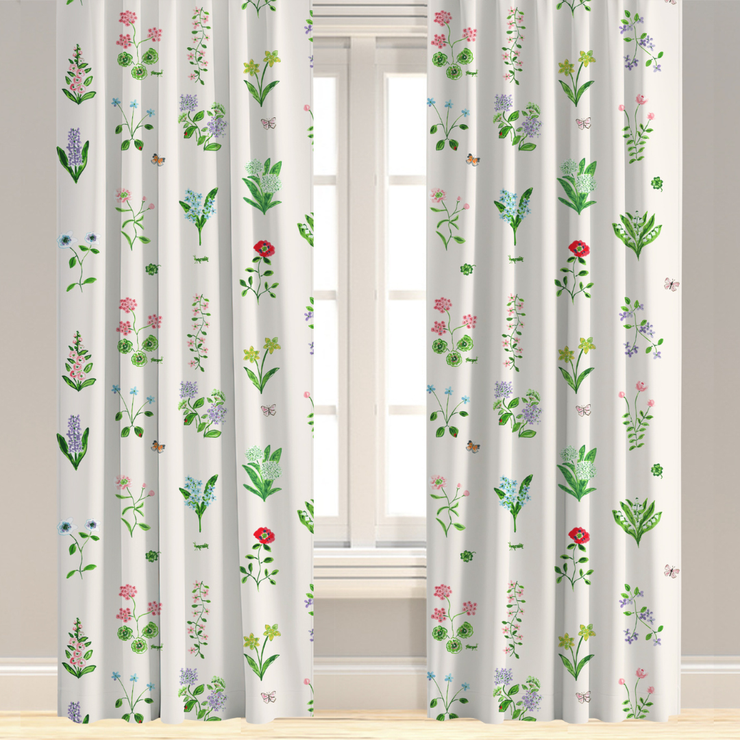 A white drapery panel with a colorful floral pattern, hanging in a window.