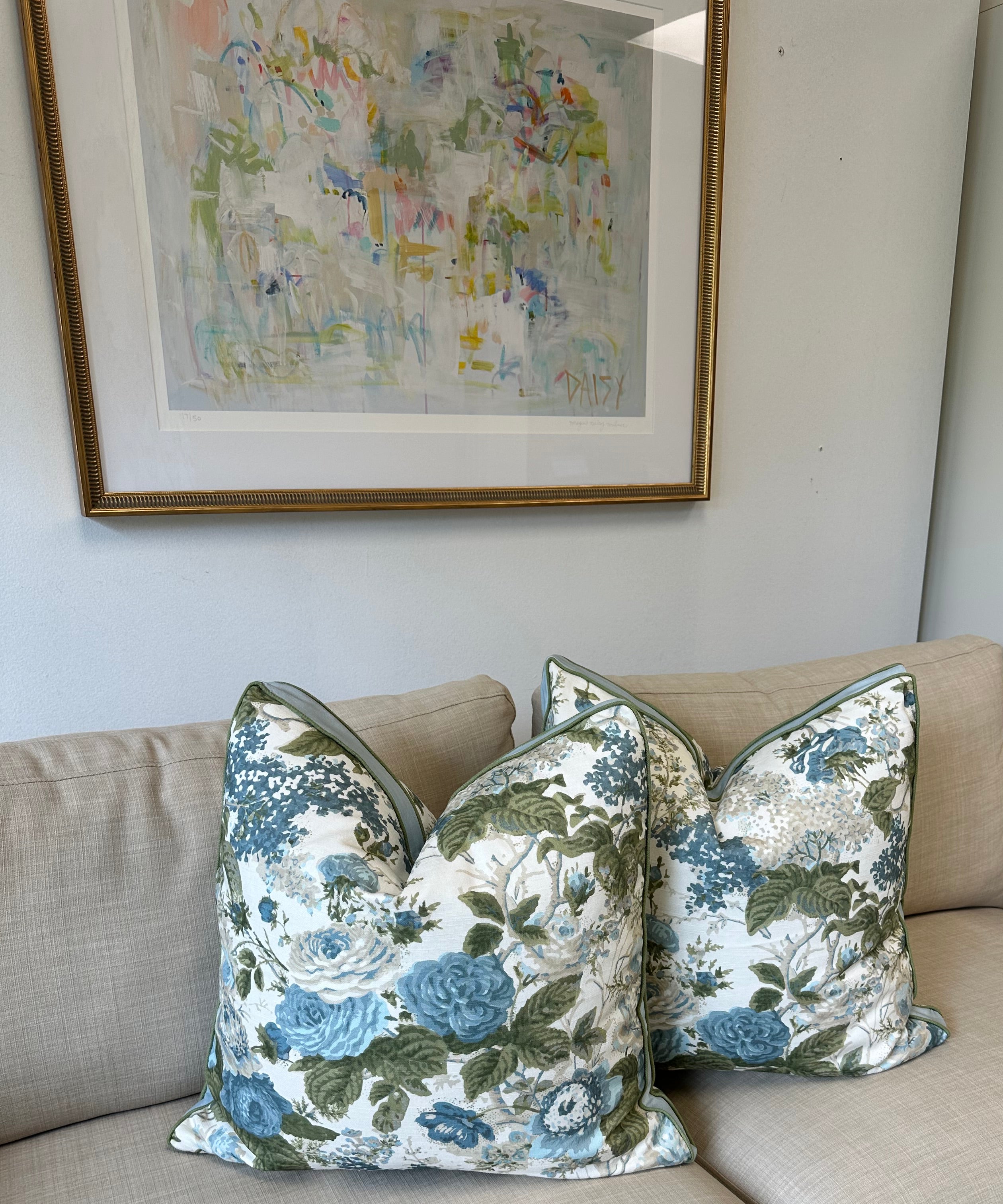 Beige sofa with floral-patterned cushions next to a framed picture on a white wall.