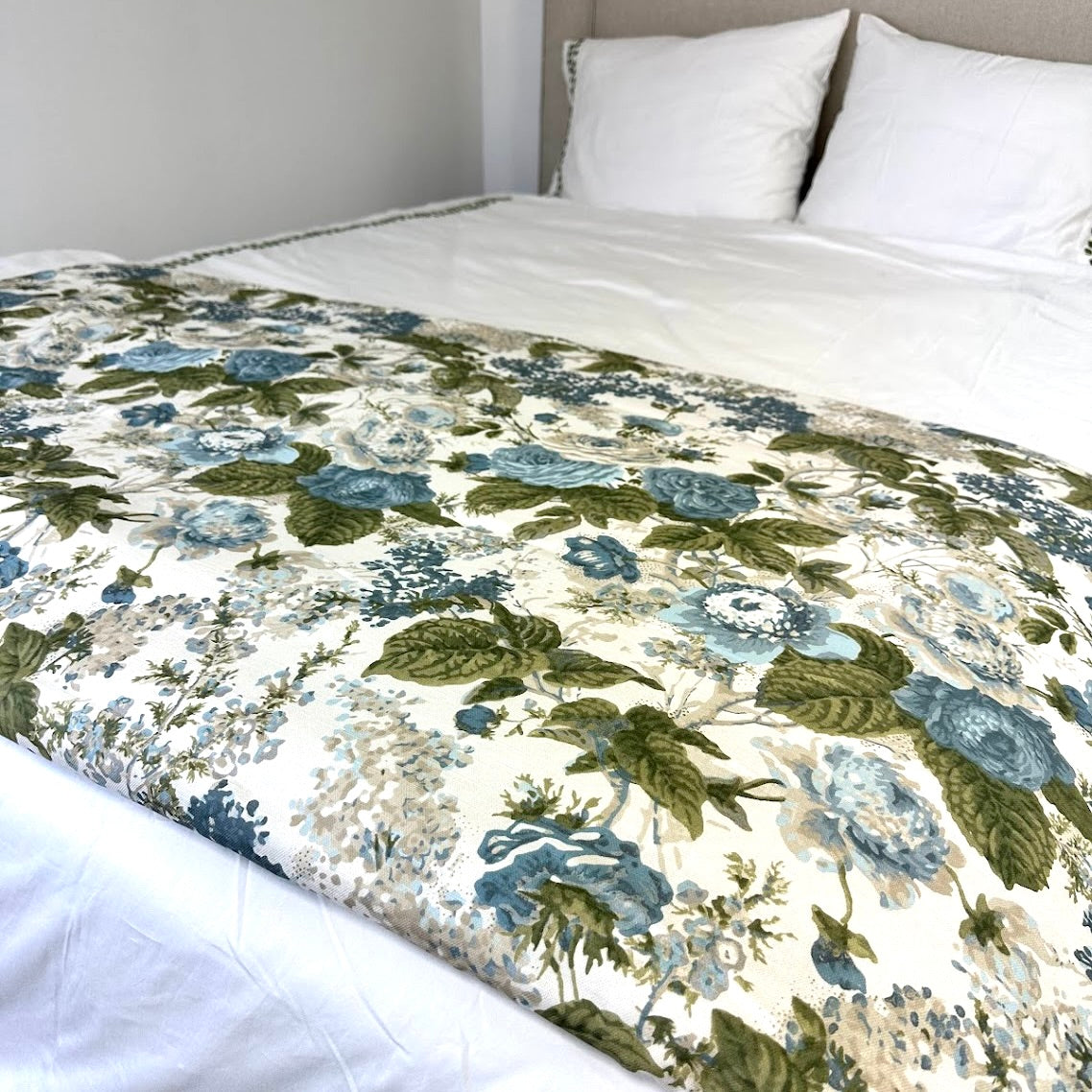 Floral patterned bed footer in green and blue on a bed with white pillows