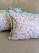 Two decorative throw pillows with a pink and green floral trellis pattern and striped green ruffled trim, resting on a beige textured fabric sofa.