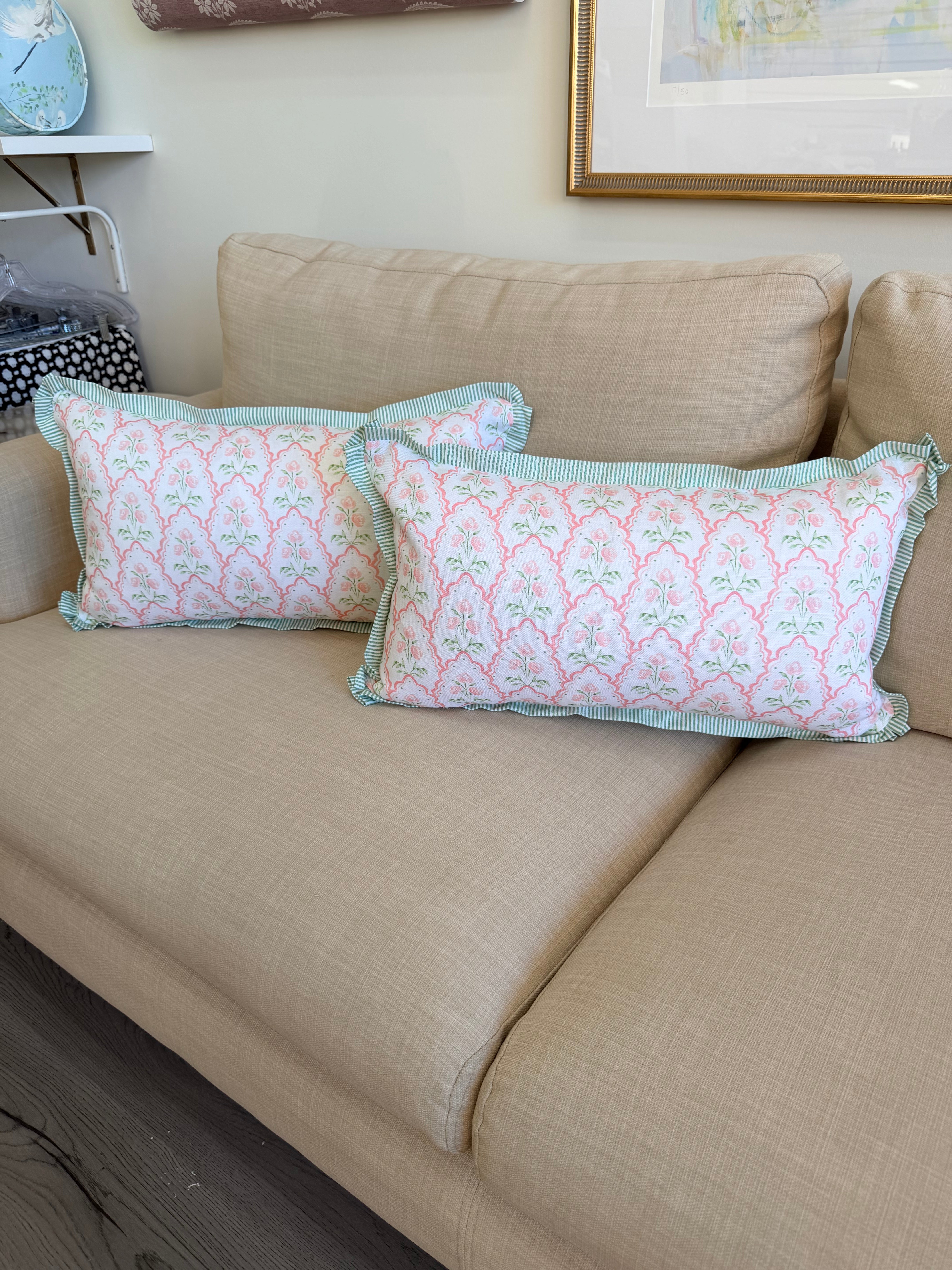Two decorative throw pillows with a pink and mint green damask pattern and light blue-green ruffled trim, displayed on a beige fabric sofa.