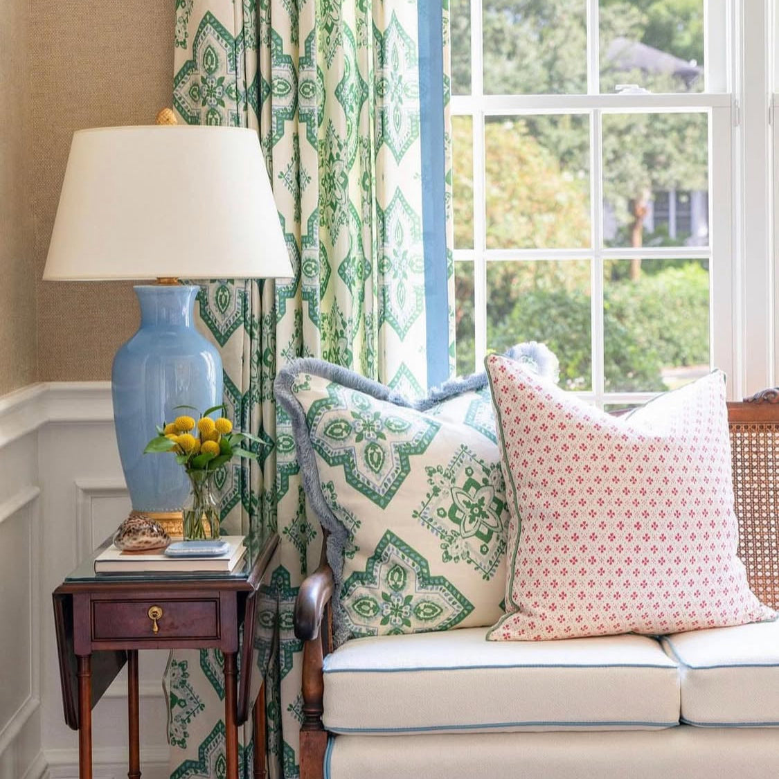 Living room with a sofa, lamp, and decorative pillows near a window with patterned curtains.