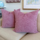 Two textured dusty rose throw pillows resting on a beige fabric sofa in a styled living room setting.
