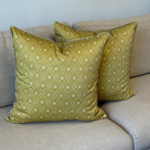 Green patterned pillows on a beige sofa with a framed picture in the background.