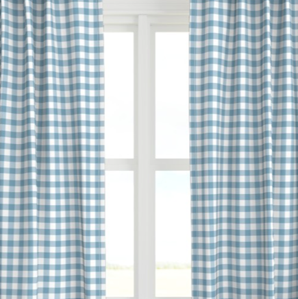 A set of blue and white checkered drapery panels hanging on a window, with the light from the window illuminating the fabric.