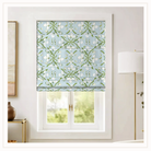 A light blue Roman shade with a white floral and green vine pattern by Evelyn Henson, shown installed on a window in a bright, modern room.