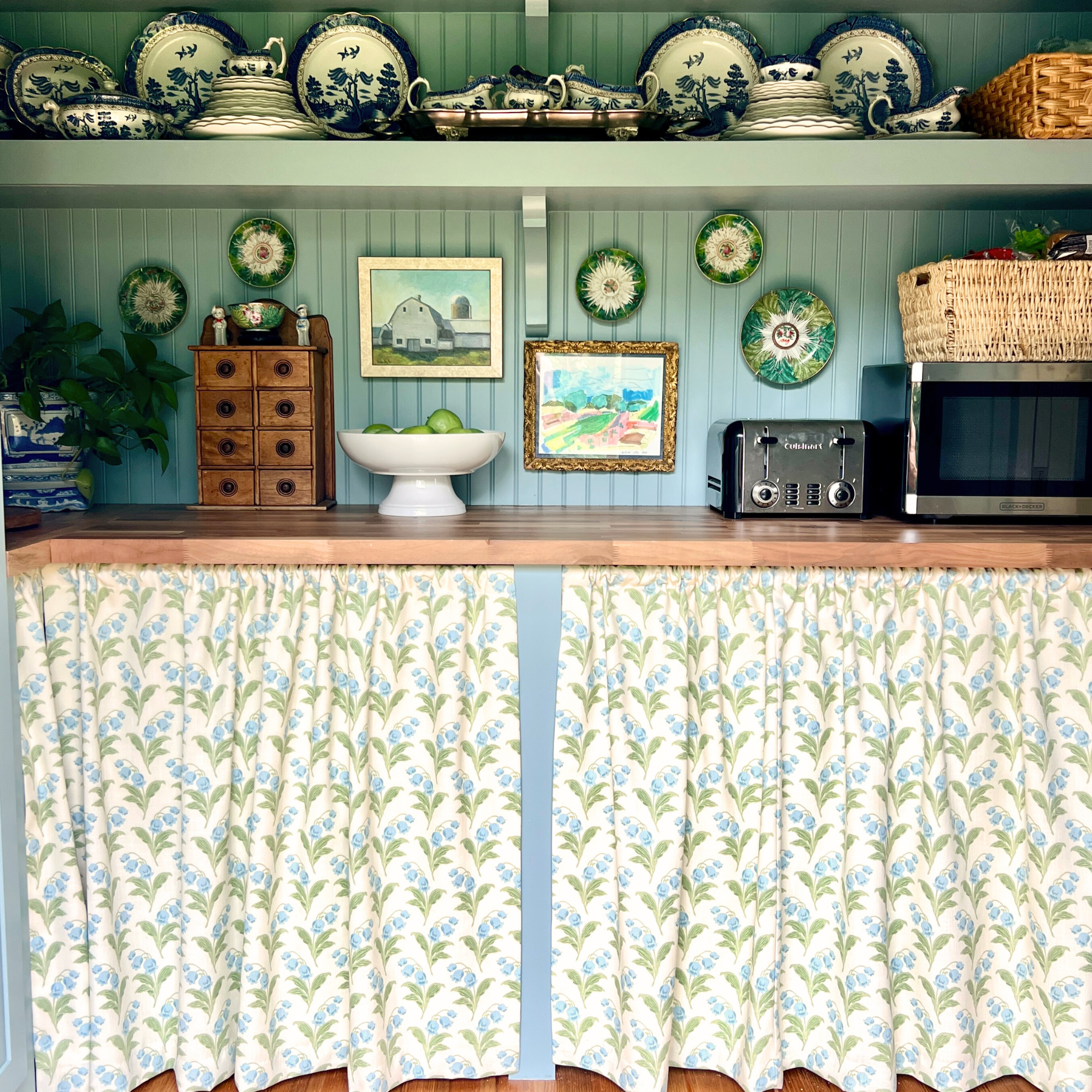 Kitchen interior with floral curtains, wooden cabinets, and decorative items.