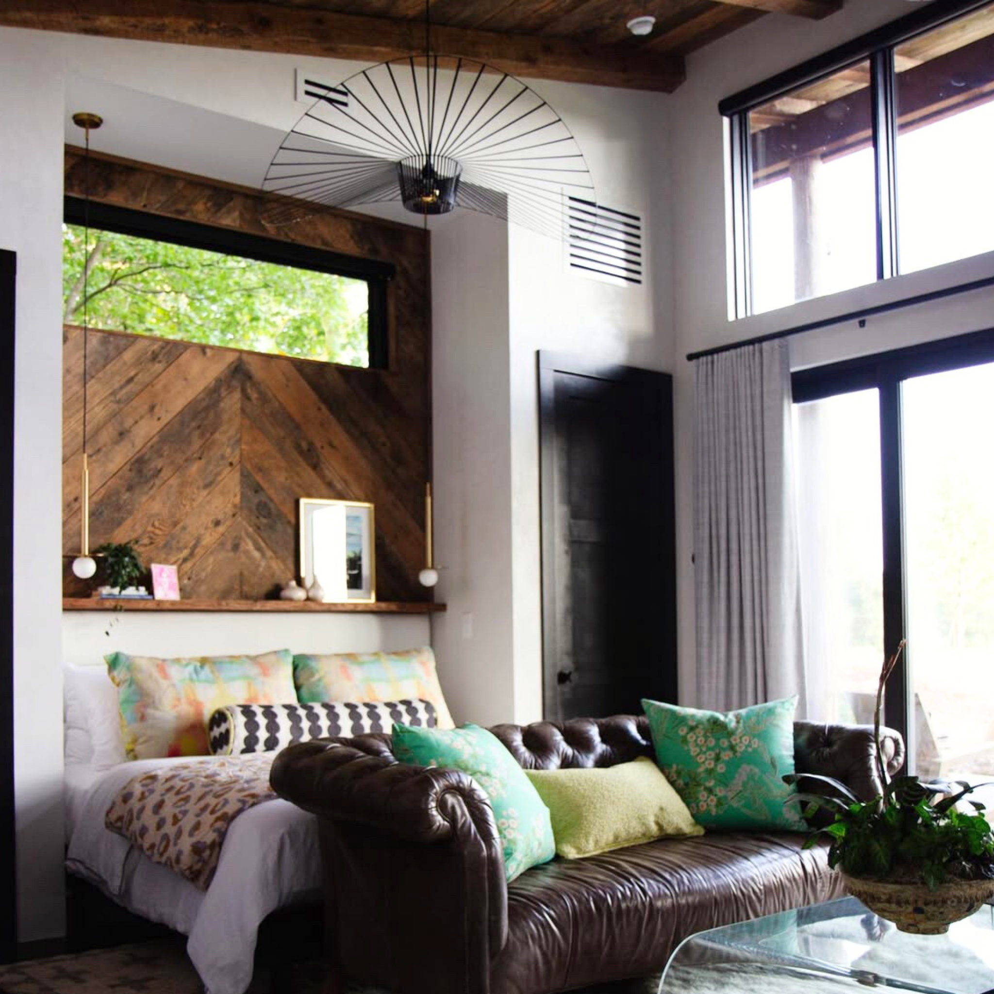 Living room with a brown leather sofa, colorful pillows, and large windows.