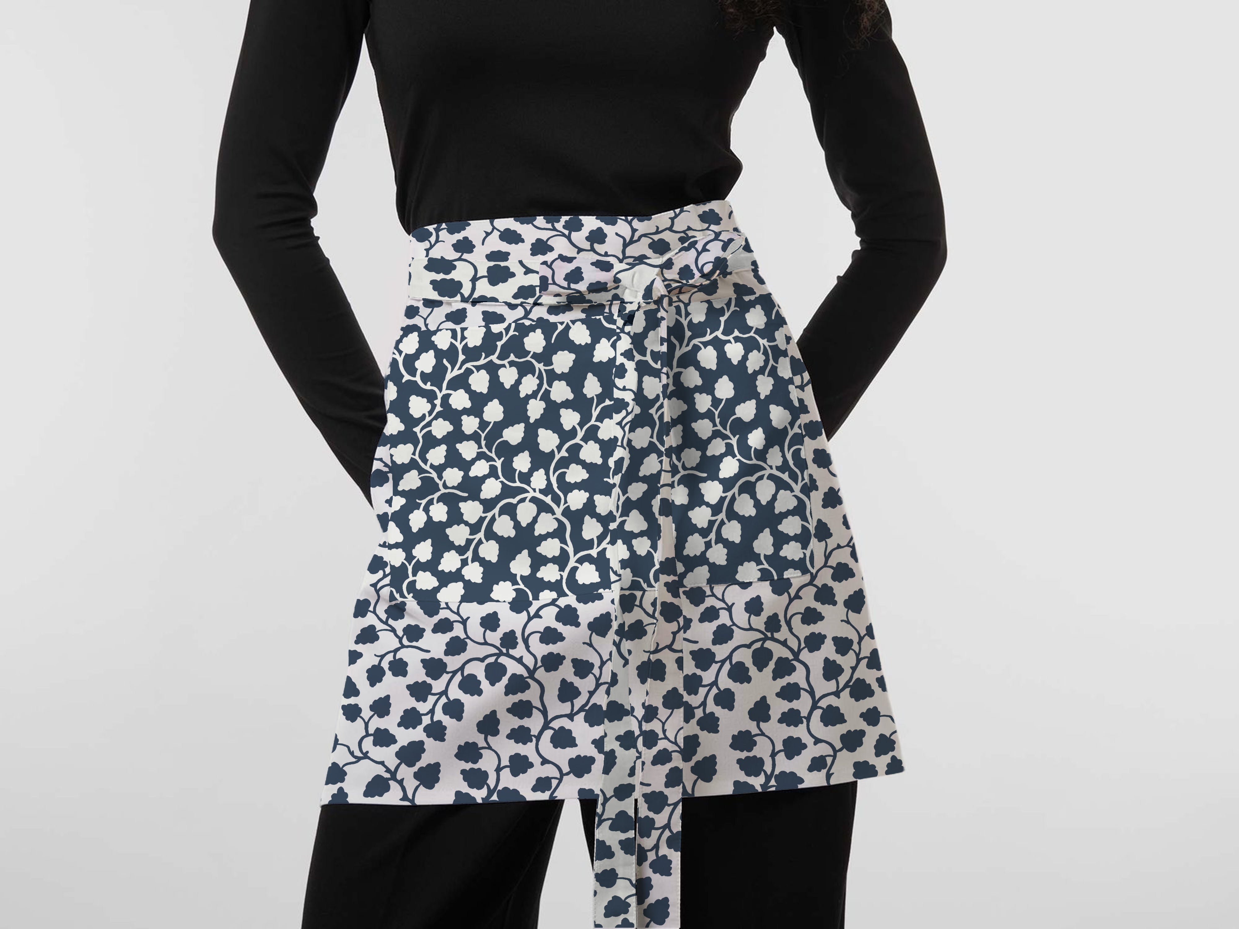 Woman wearing a navy and white floral apron featuring exclusive Wheaton Whaley Home patterns and colorways.